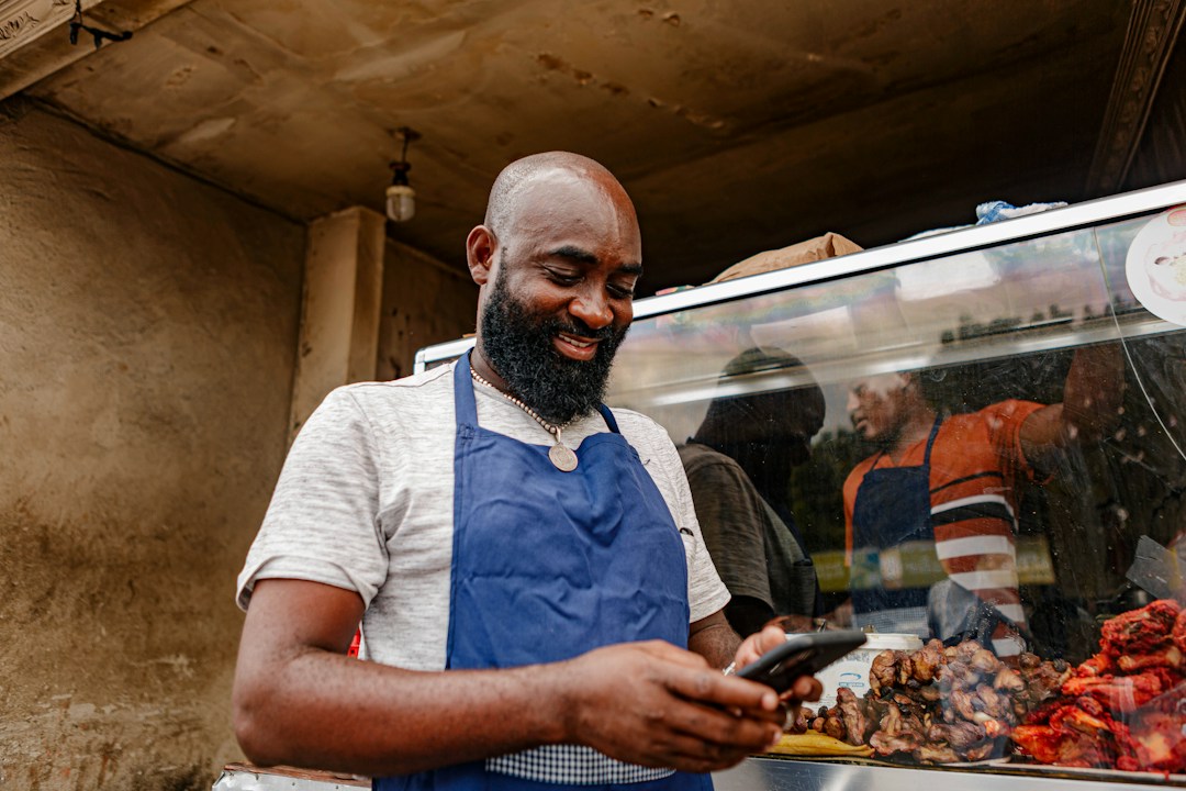 A Black local food vendor using a smartphone to support his business